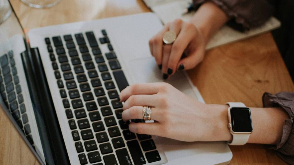 A photo of a women with rings on her fingers using a laptop