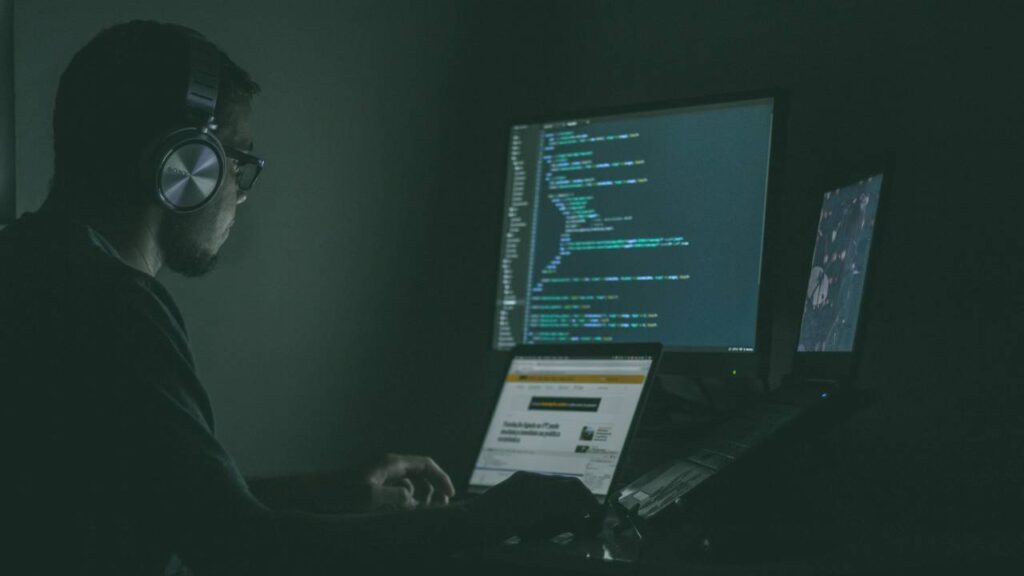 Man using several computers at once in a dark room 