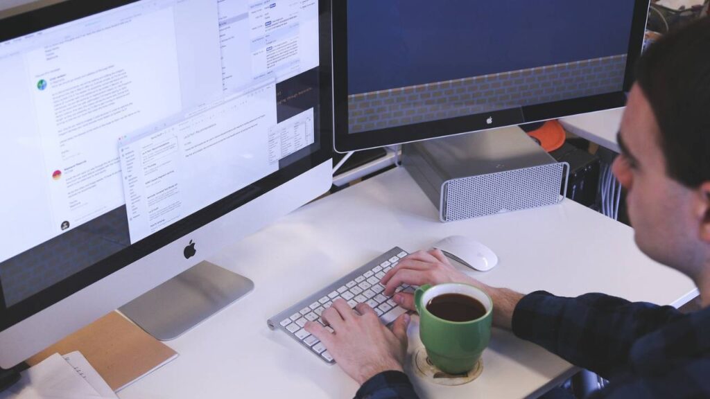 An employee having a cup of coffee while using his Apple desktop computer 