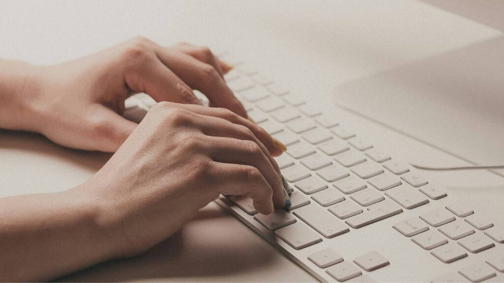 A close-up photo of a woman using a white Apple keyboard 